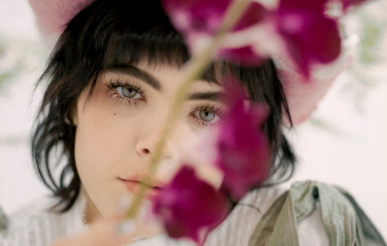 BENEE with pink flowers over her eyes a press shot