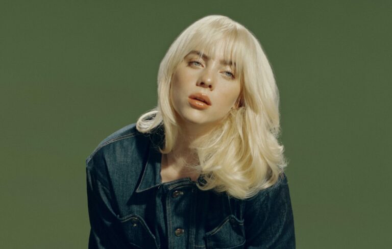 Billie Eilish poses for a press picture wearing a shirt in front of a green background