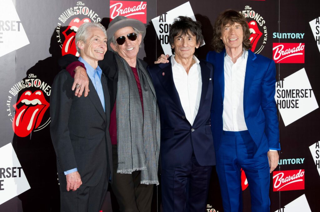The Rolling Stones pose in front of a wall of their logo