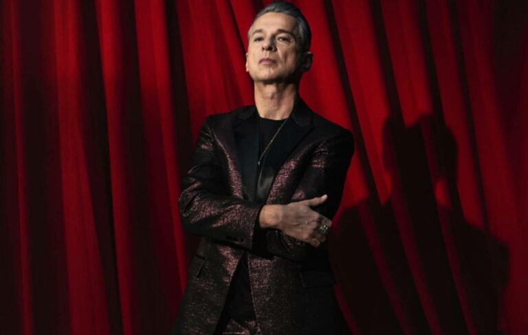 Dave Gahan standing in front of a red curtain