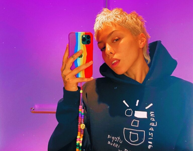 Poppy poses with her phone in the mirror against a purple background