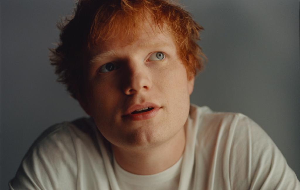 Ed Sheeran looks up and wears a white t-shirt in a press shot