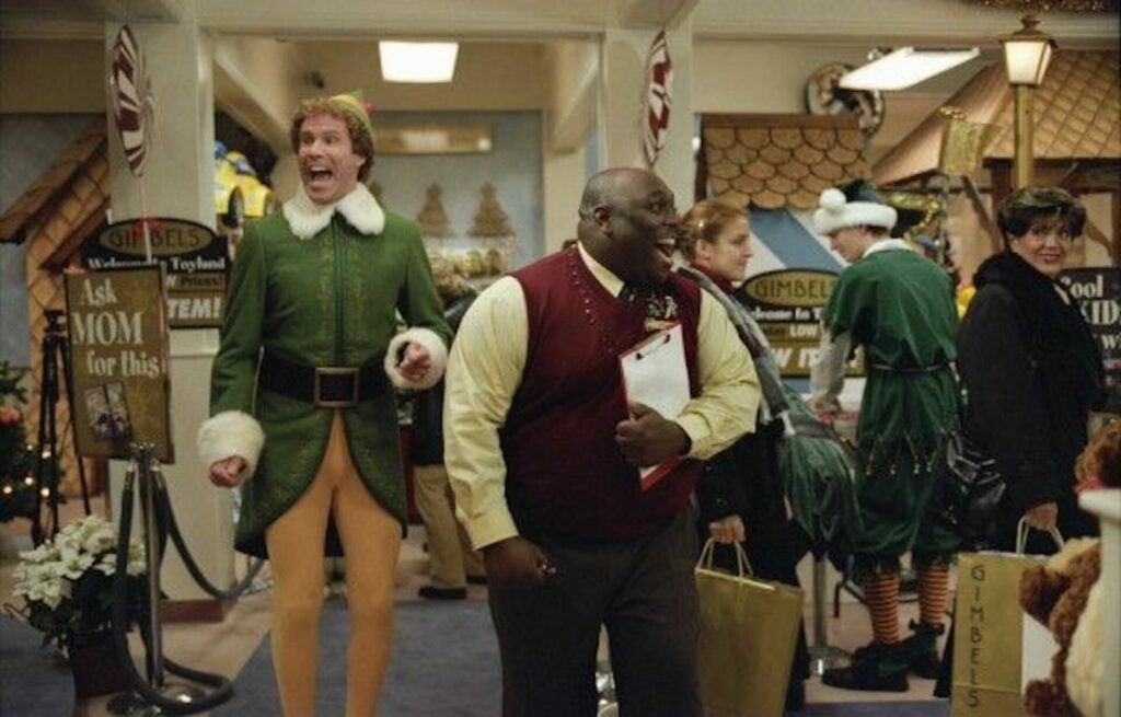 Will Ferrell as Buddy the elf (left) with Faizon Love who played the shop's manager (right). Love shouts at the staff whilst Ferrell's character screams in excitement