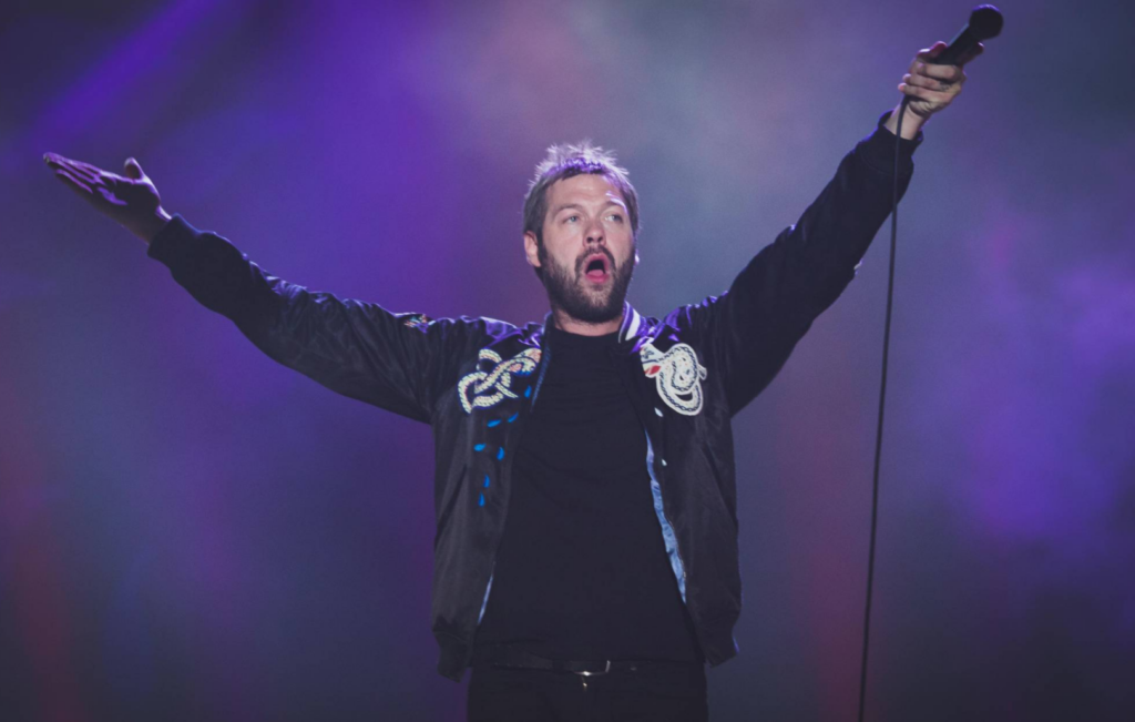 Tom Meighan stands with his arms up in a live performance