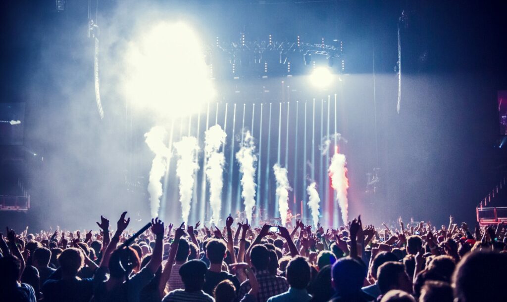 A picture of a group of people watching a concert is taken from the back