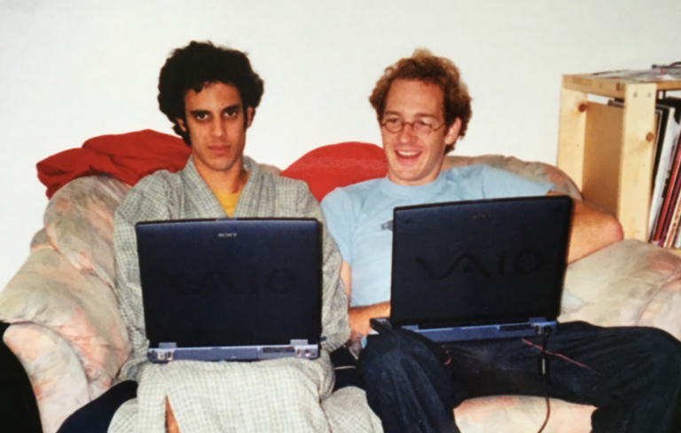 Four Tet and Caribou sit together on a sofa on laptops