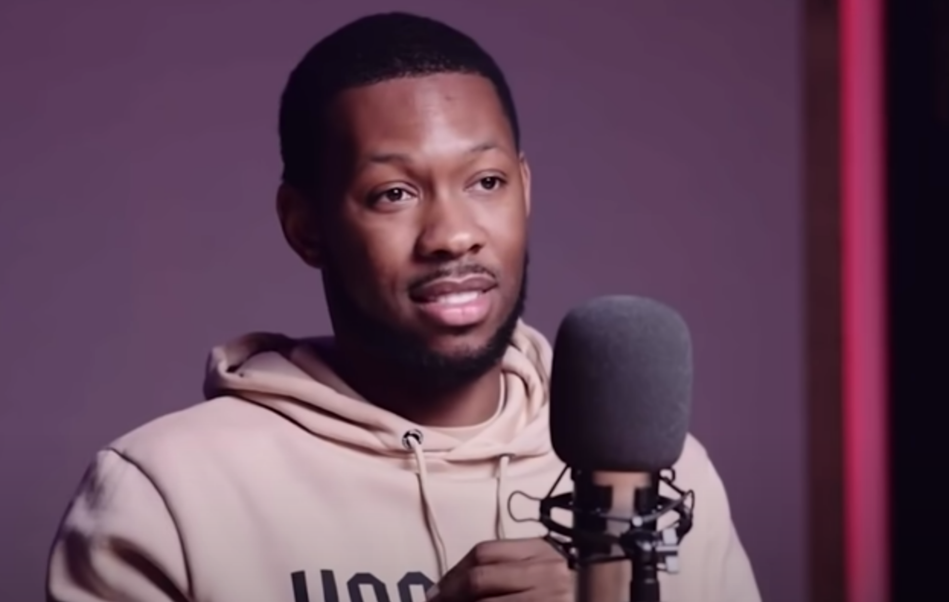 Fumez The Engineer sits in front of a microphone and wears a beige hoody