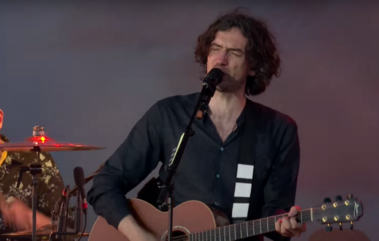 Gary Lightbody wears a navy blue shirt and plays a guitar in front of a microphone