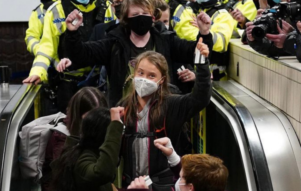 Greta Thunberg waves on an escalator surrounded by crowds as she arrives in Glasgow