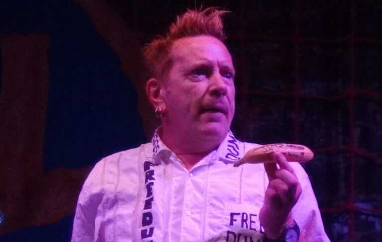 John Lydon is pictured holding a sausage on stage