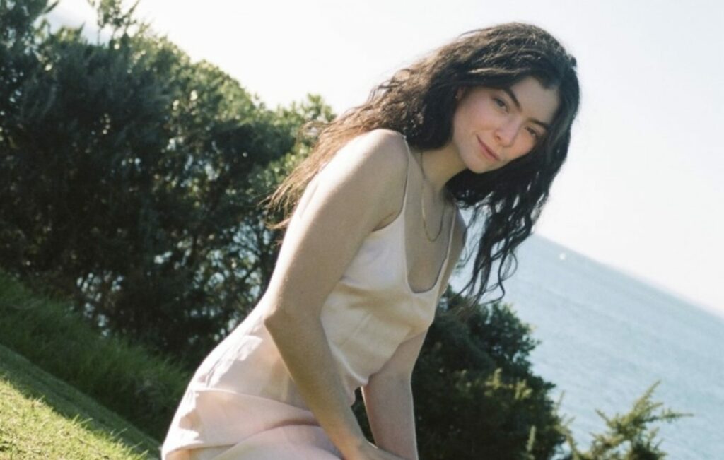 Lord poses in a silky dress in front of greenery and the sea