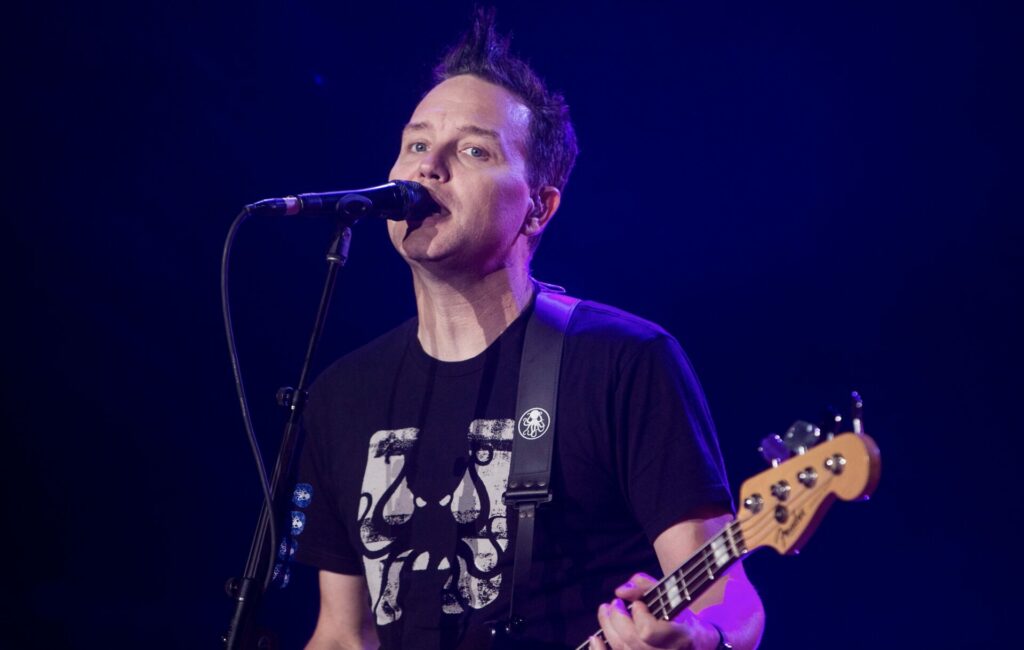 Mark Hoppus performing live in front of a microphone and holding a bass