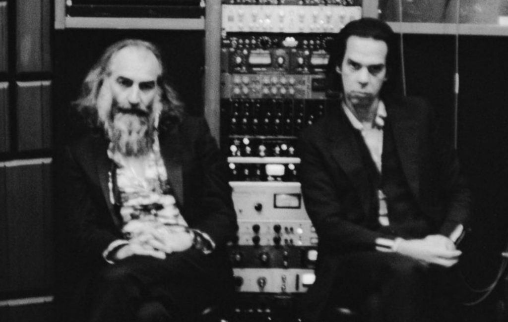Nick Cave Warren Ellis sit against computer gear in a black and white photo