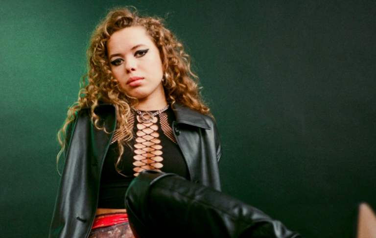 Nilüfer Yanya wears a black leather jacket and laced up top against a green background
