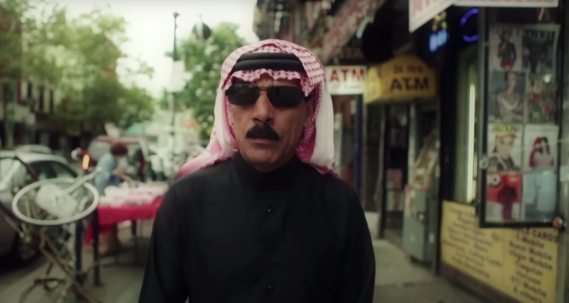 Omar Souleyman wears a red and white checkered headscarf and sunglasses in the music video for Warni Warni