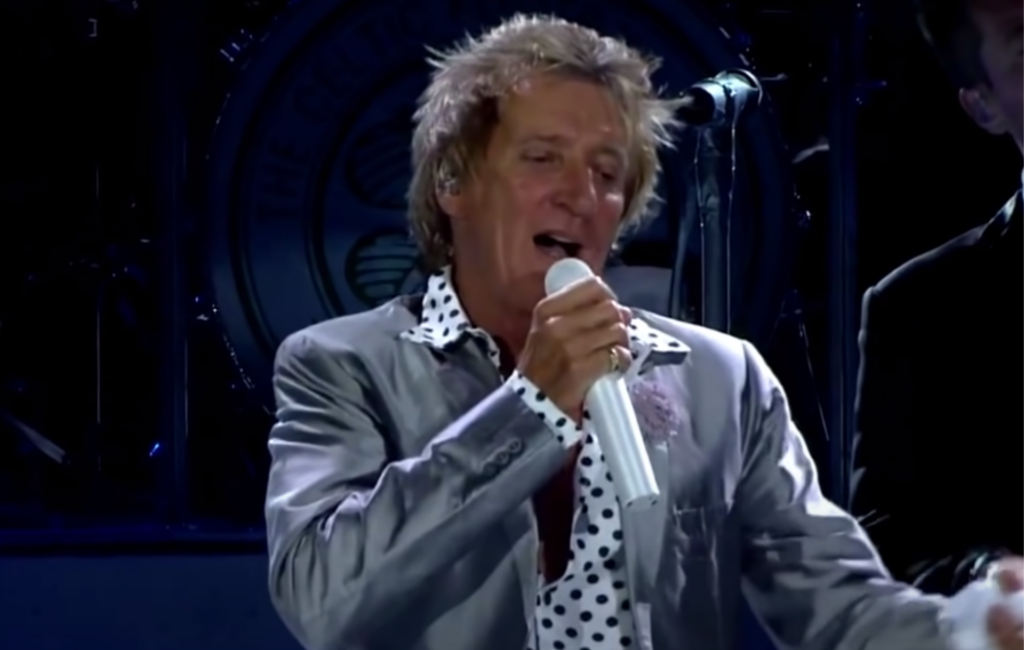 Rod Stewart wears a silver jacket and polka dot shirt performing live