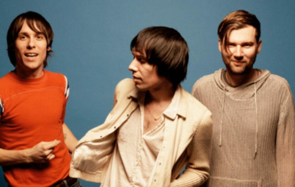 Press picture of The Cribs stood in front of a blue background.