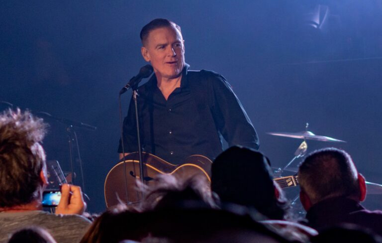 Bryan Adams is seen wearing a black shirt and performing live