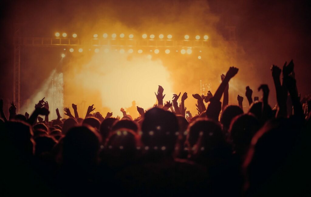 Photo of an audience with their hands up in front of a stage with yellow light