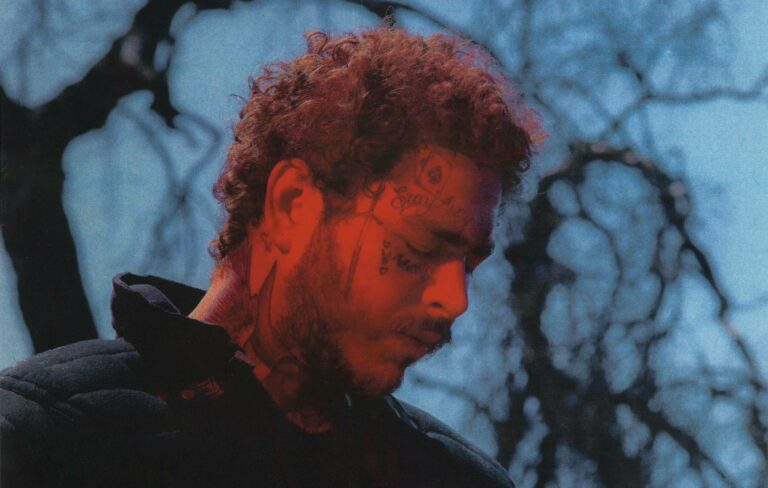 Post Malone poses in front of some trees with red light illuminating his face