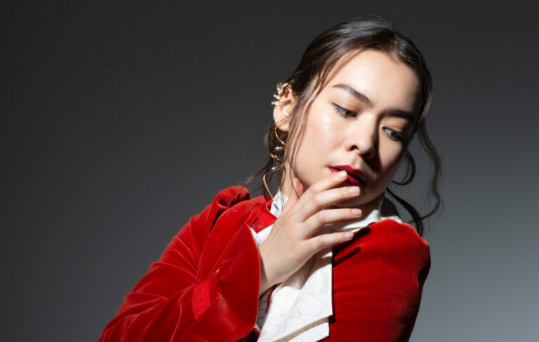 Mitski posing and looking to the ground in a red jacket