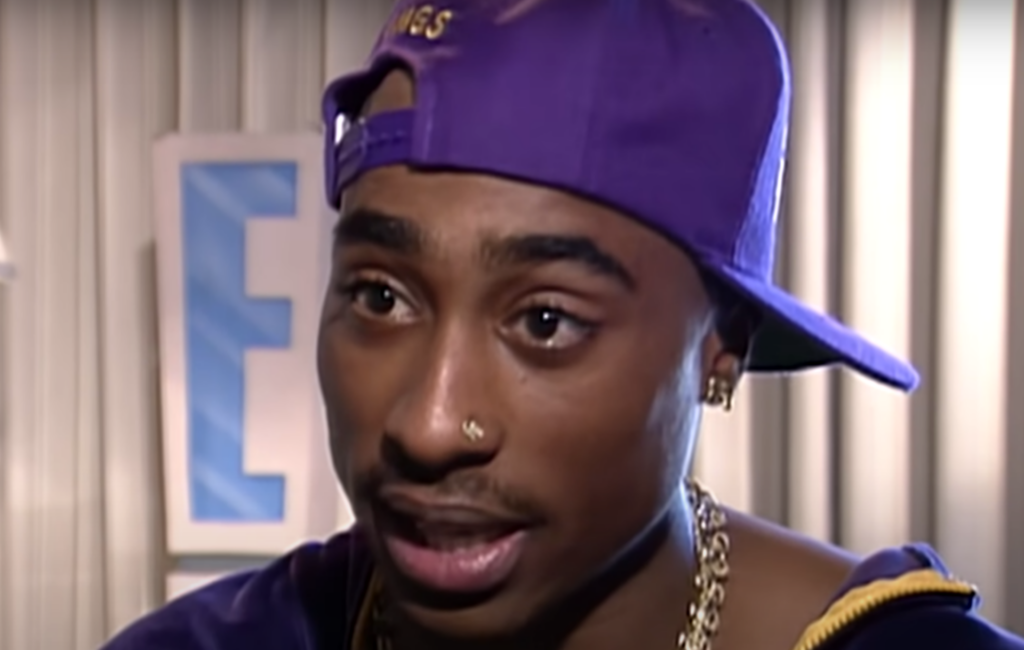 Tupac Shakur wears a purple backwards cap and gold chain in an interview