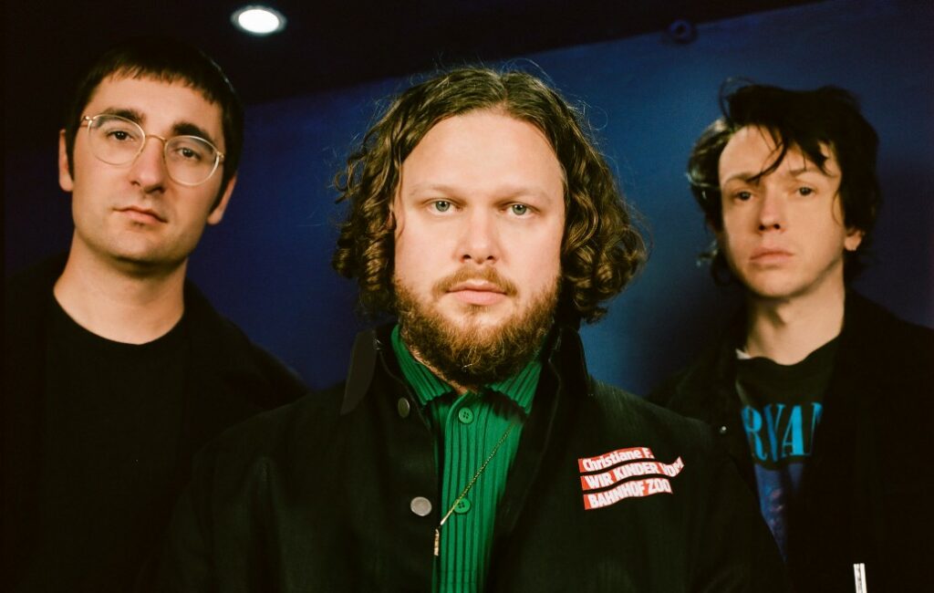 Members of alt-J look directly at the camera against a blue background