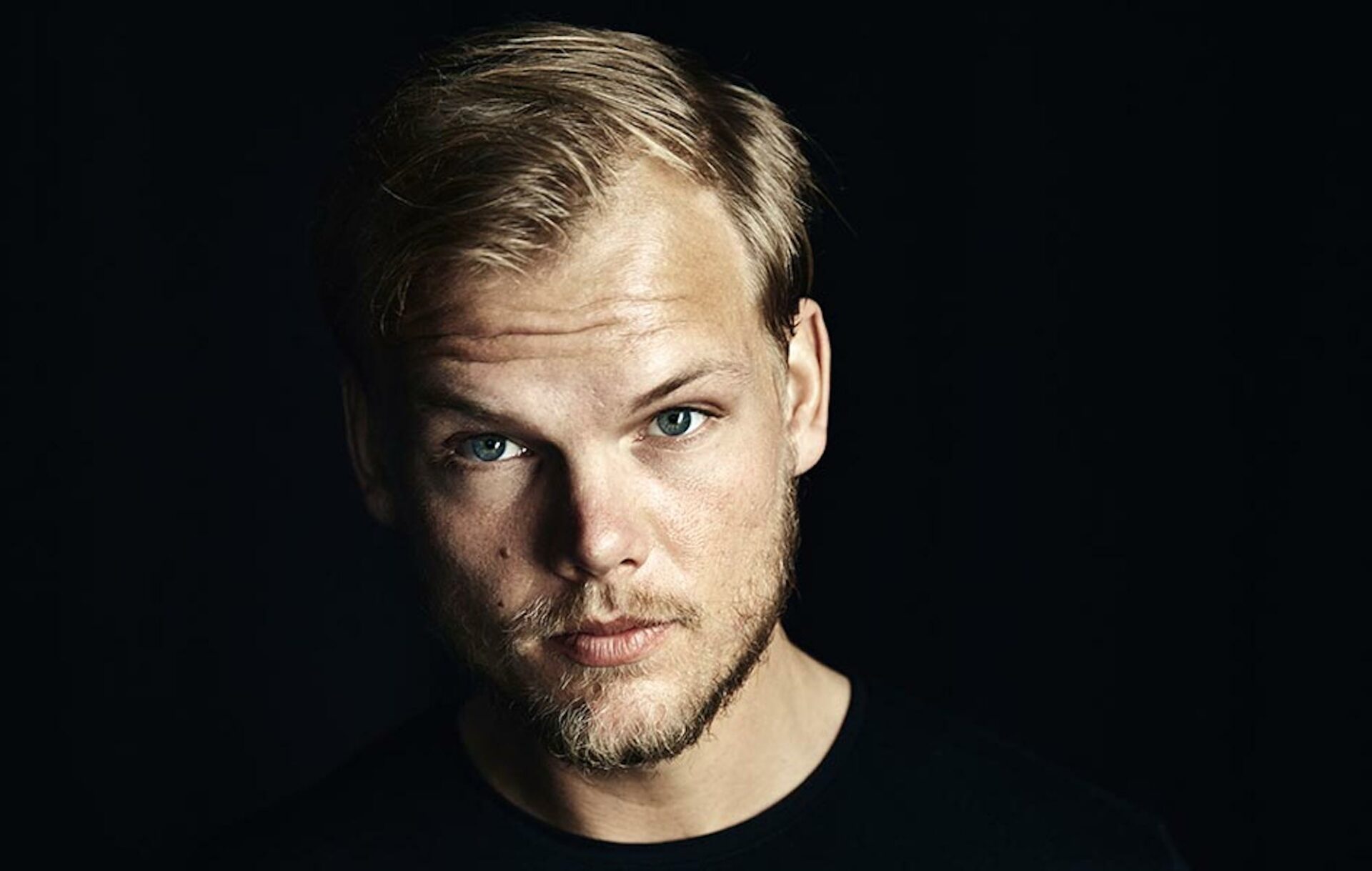 Avicii posing for the camera against a dark background