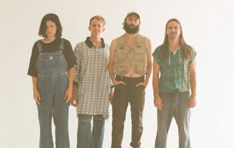 The four members of Big Thief standing side by side posing for the camera against a white background