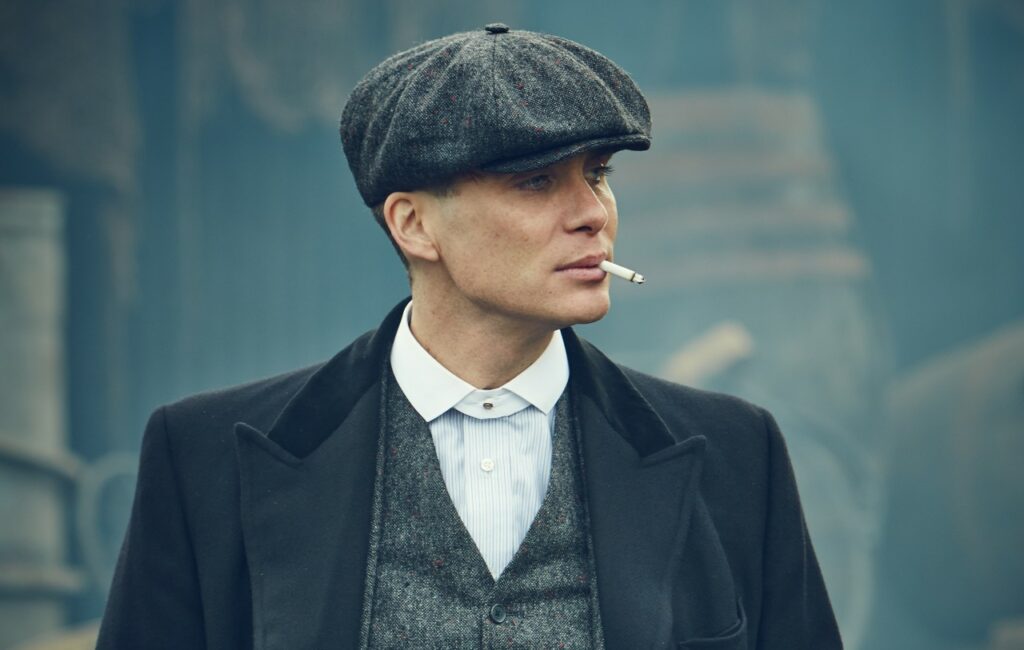 Cillian Murphy plays Tommy Shelby in 'Peaky Blinders', wearing a cap and smoking a cigarette