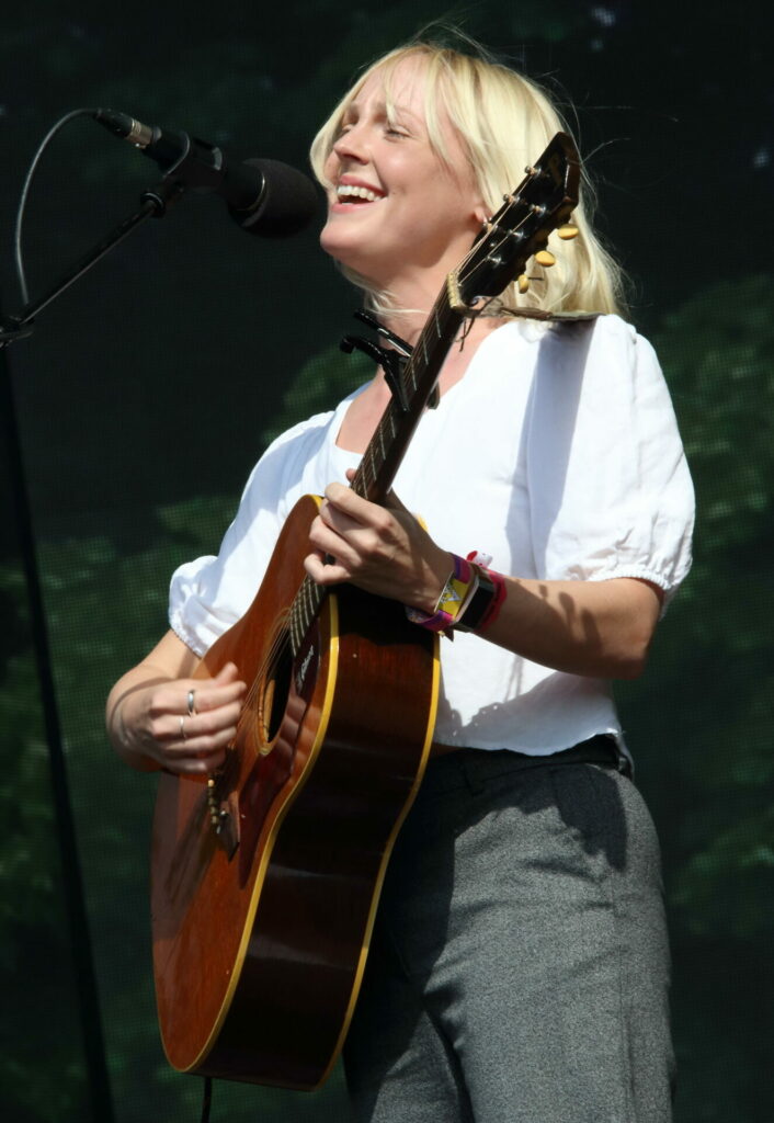 Laura Marling performs live in London holding a brown acoustic guitar and wearing a white shir