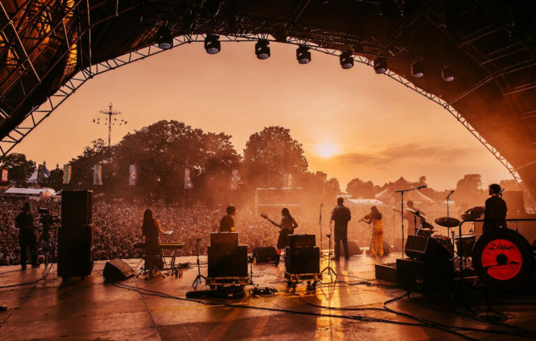 View of a festival stage at sunset while seven musicians play in a line