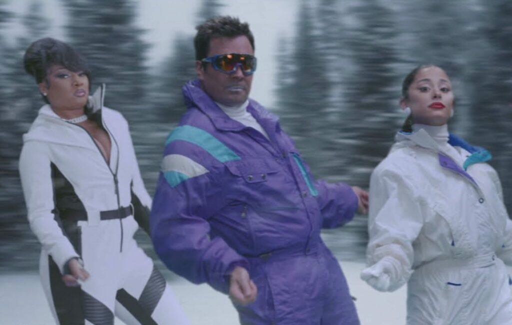 Ariana Grande, Megan Thee Stallion and Jimmy Fallon standing side by side in snow gear in front of a snowy forest