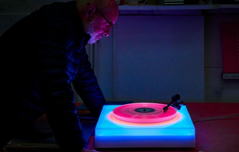Brian Eno looking at a multicoloured vinyl turntable