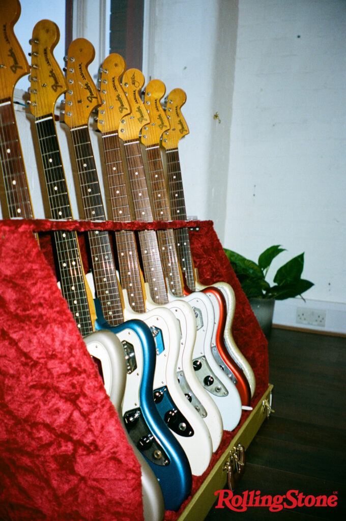 A row of different coloured guitars in a red velvet rack