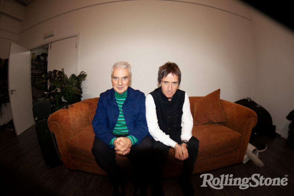 Johnny Marr and Jon Savage sit together on a brown sofa against a white background