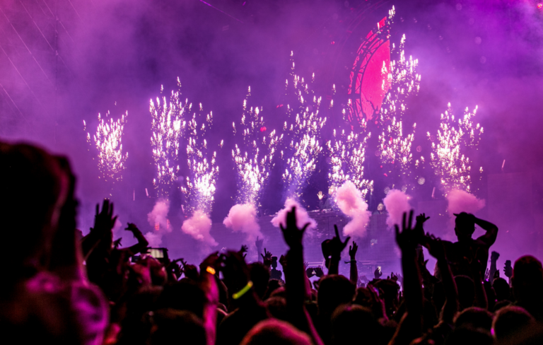 A crowd raises their hand in front of a live performance with smoke and pyrotechnics