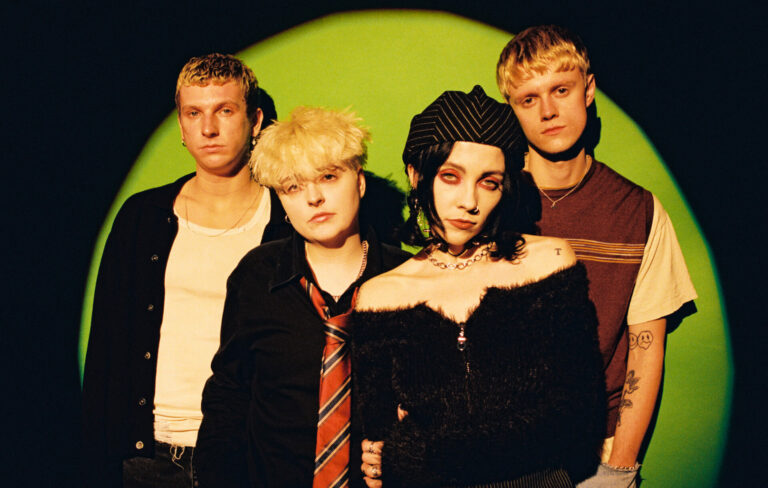Pale Waves pose for the camera in front of a green background