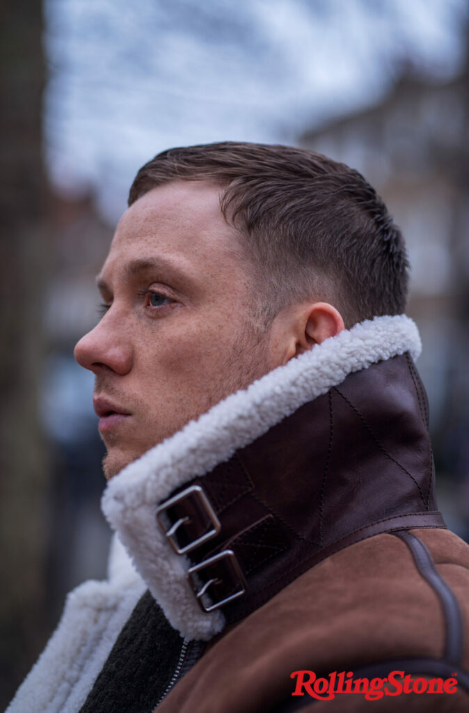 Joe Cole wears a brown leather, fur lined coat in a side profile photo