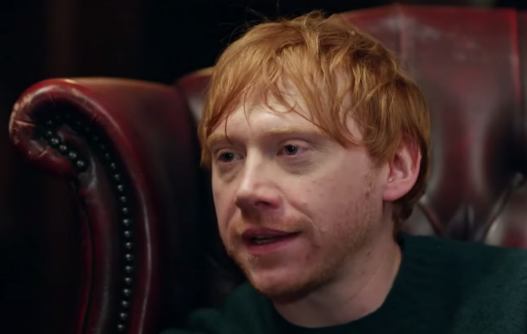 Rupert wears a dark shirt on a red leather chair