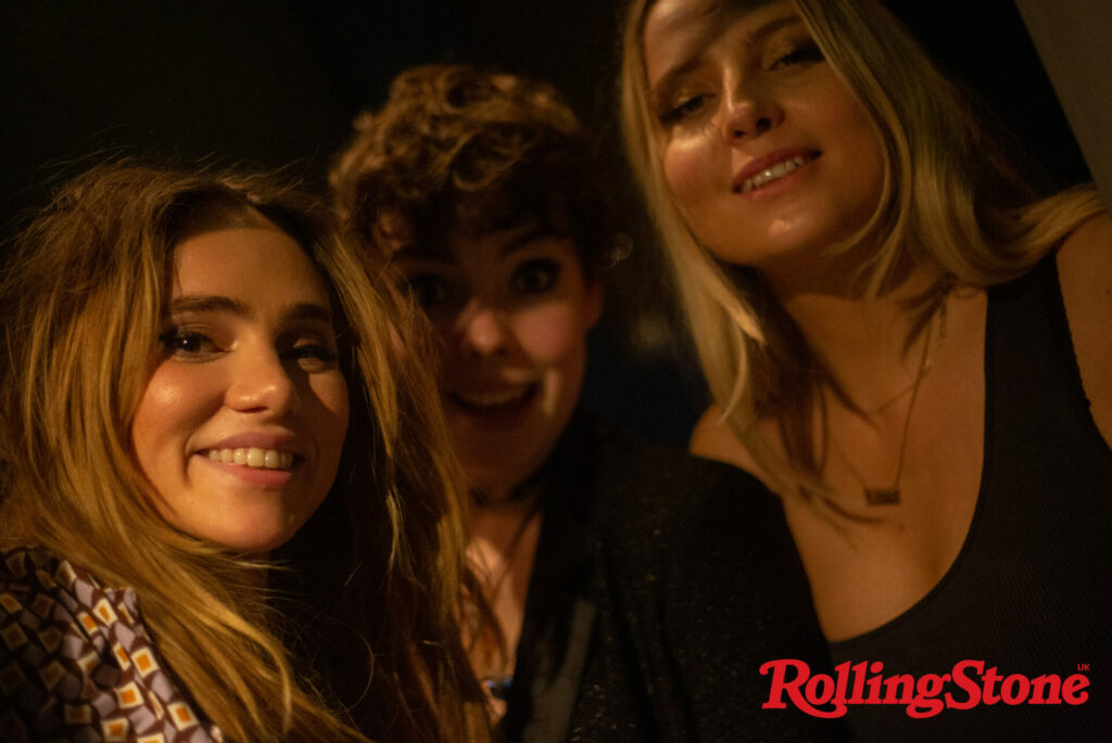Suki Waterhouse smiles with two others backstage