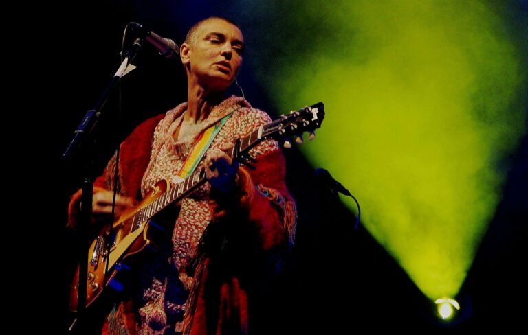Sinead O'Connor performs live with a guitar hung on a rainbow strap