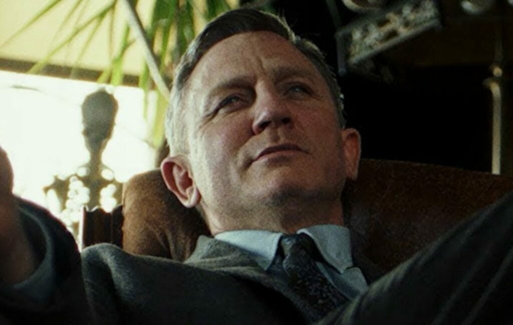 Daniel Craig leans back on a sofa wearing a suit in 'Knives Out'