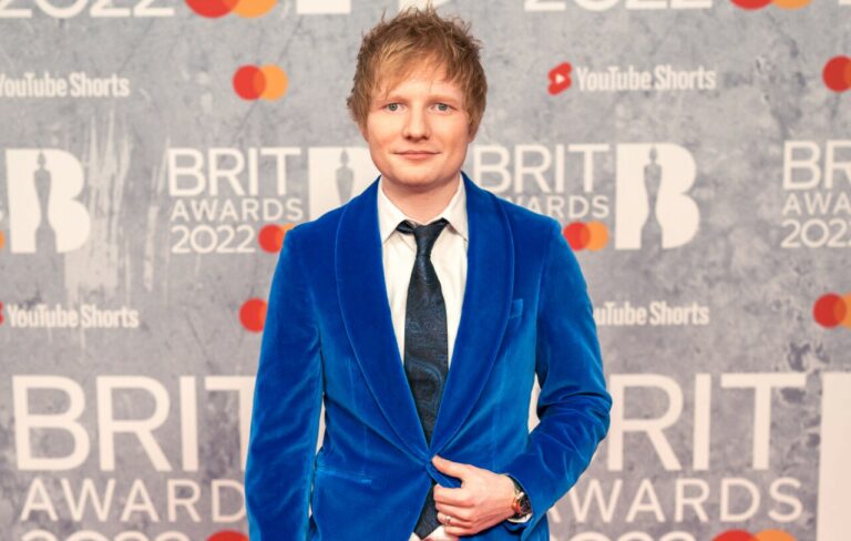 Ed Sheeran wears a blue velvet suit and dark blue tie against the BRIT Awards backdrop