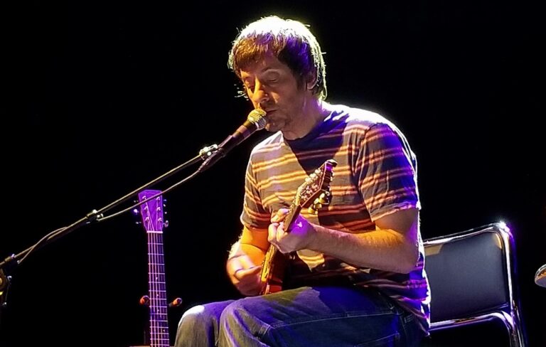 Graham Coxon sits on stage while playing the guitar