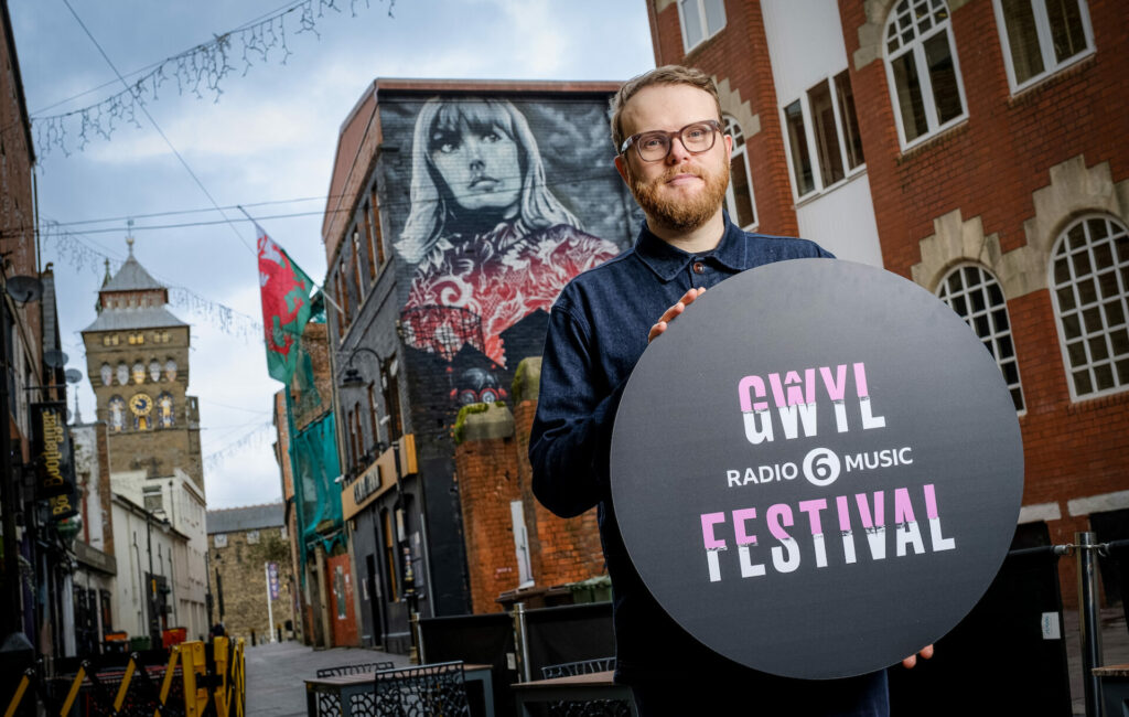 Huw Stephens holds up a sign in Cardiff announcing the 2022 BBC Radio 6 Music Festival