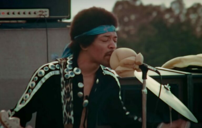 Jimi Hendrix performs liv in a green shirt and blue headband in 1970