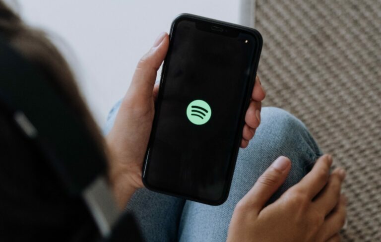 A person holds their smartphone with the Spotify icon on the screen