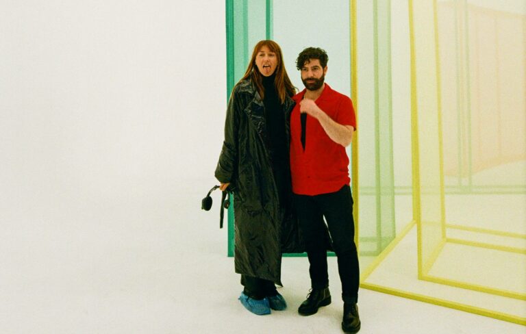 Tanu Muiño and Yannis Philippakis standing next to perspex boxes on a video set in a studio