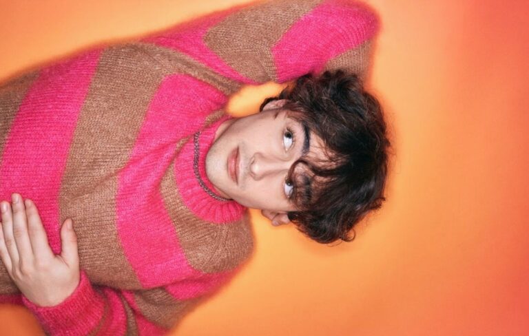 Alfie Templeman poses in a pink and brown striped jumper